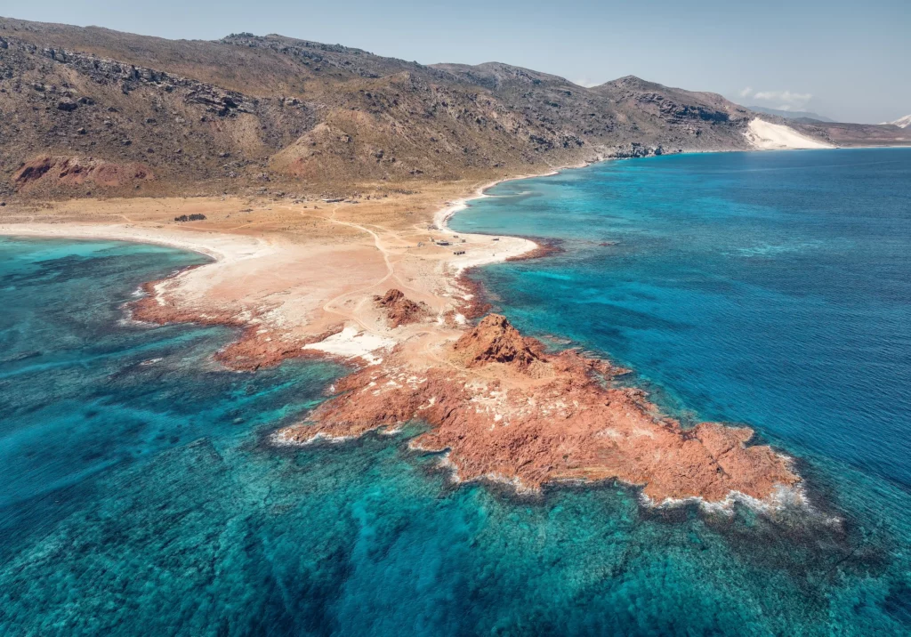 Aerial view of a rocky coastline with red outcrops and turquoise waters along a remote beach